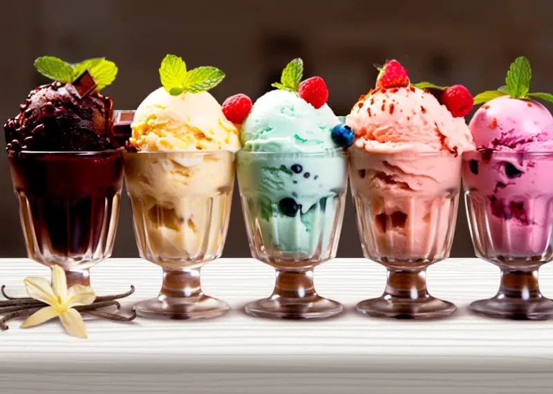 5 Copas servidas con helados de diferentes sabores, una balanza y un litro de leche como portada del artículo Fabricación de helado